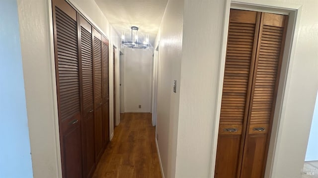 hallway featuring dark wood-type flooring, a textured ceiling, and an inviting chandelier