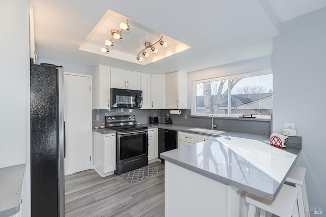 kitchen with kitchen peninsula, a raised ceiling, sink, black appliances, and white cabinetry