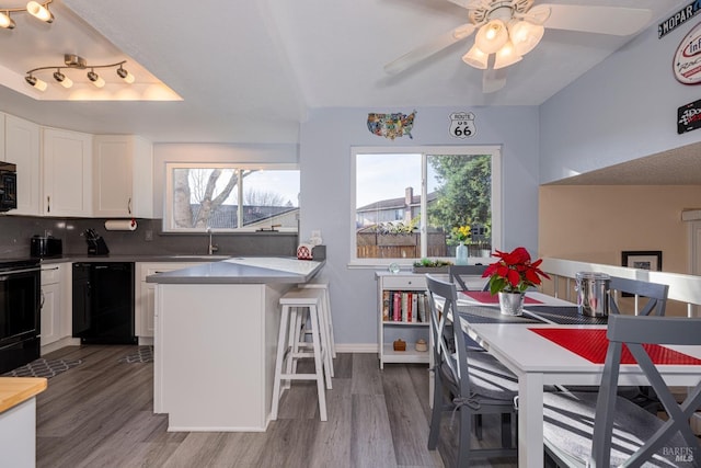 kitchen featuring backsplash, black appliances, wood-type flooring, a kitchen bar, and white cabinetry