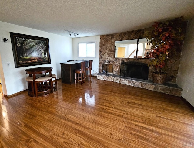 living room featuring a stone fireplace, wood-type flooring, and a textured ceiling