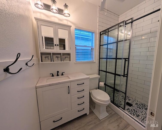 bathroom featuring wood-type flooring, tiled shower, vanity, and toilet