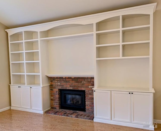 unfurnished living room featuring wood-type flooring and a brick fireplace