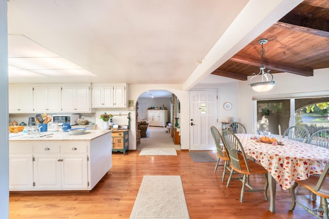 kitchen with arched walkways, beamed ceiling, light countertops, white cabinets, and light wood-type flooring