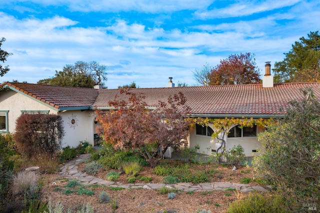 back of house with a chimney, stucco siding, and a tile roof