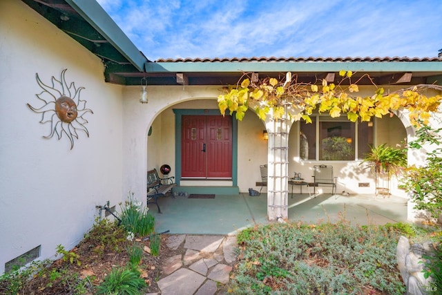 view of exterior entry featuring stucco siding, covered porch, and a tiled roof