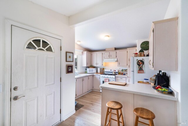 kitchen with a breakfast bar, kitchen peninsula, cream cabinets, white appliances, and light hardwood / wood-style flooring