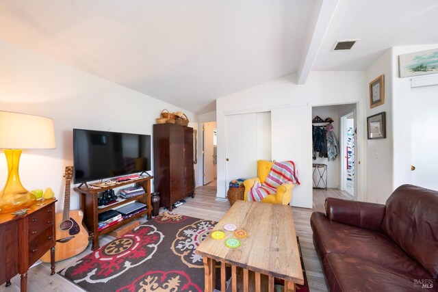 living area featuring wood finished floors, lofted ceiling with beams, and visible vents
