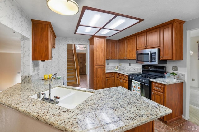 kitchen with black gas range, kitchen peninsula, light stone counters, and sink