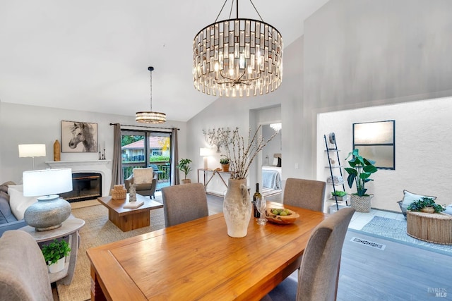 dining room featuring a glass covered fireplace, an inviting chandelier, wood finished floors, and high vaulted ceiling