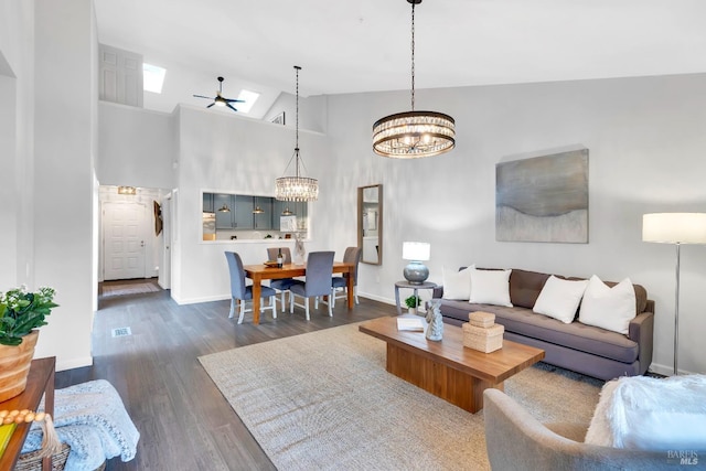 living area featuring visible vents, baseboards, ceiling fan with notable chandelier, dark wood-style floors, and high vaulted ceiling