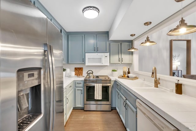 kitchen with tile countertops, light wood-type flooring, appliances with stainless steel finishes, blue cabinets, and a sink