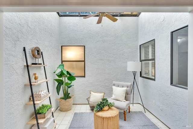 living area featuring tile patterned flooring, a ceiling fan, and a textured wall