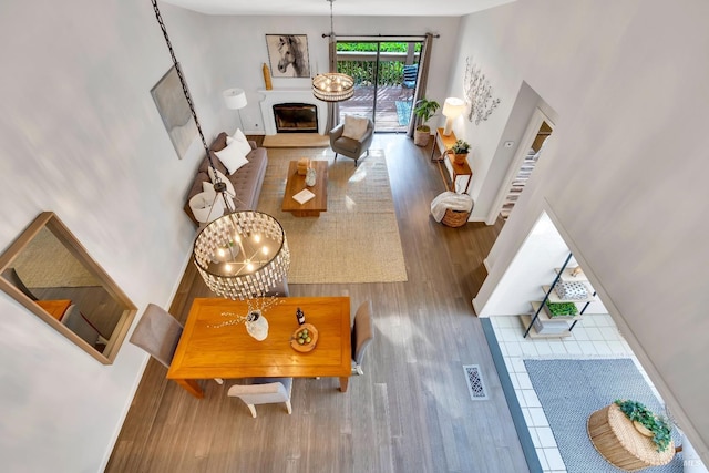 living area featuring wood finished floors, baseboards, a towering ceiling, a glass covered fireplace, and a notable chandelier