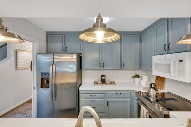 kitchen with white microwave, tile counters, decorative backsplash, stove, and stainless steel fridge