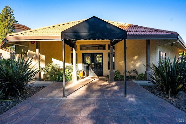 back of house featuring a tile roof, french doors, and stucco siding