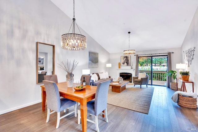 dining area with a fireplace, a notable chandelier, hardwood / wood-style floors, and high vaulted ceiling