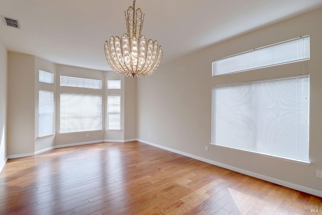 unfurnished room featuring a notable chandelier and light hardwood / wood-style flooring