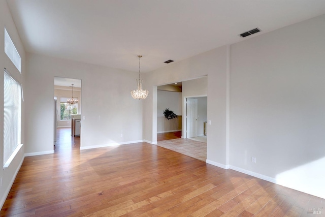 unfurnished room with a chandelier and light wood-type flooring