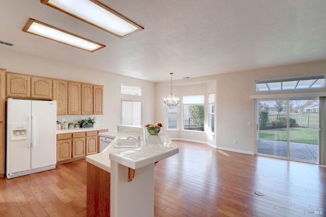 kitchen with pendant lighting, light wood-type flooring, white refrigerator with ice dispenser, and tile countertops