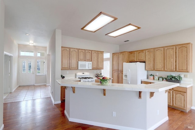 kitchen featuring a breakfast bar, white appliances, tile countertops, and light hardwood / wood-style floors