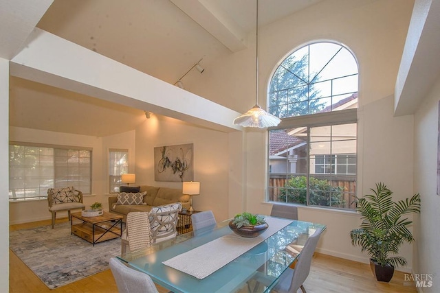 dining room with beam ceiling, light hardwood / wood-style floors, and high vaulted ceiling