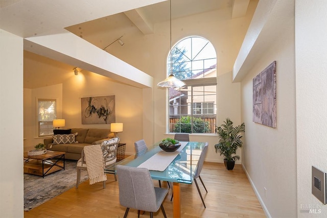 dining space with beam ceiling, high vaulted ceiling, and light hardwood / wood-style floors