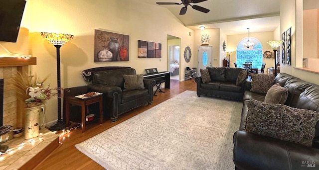 living room featuring a tiled fireplace, hardwood / wood-style floors, ceiling fan with notable chandelier, and vaulted ceiling