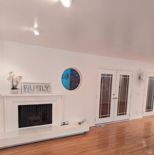 unfurnished living room with french doors, a tiled fireplace, and hardwood / wood-style floors