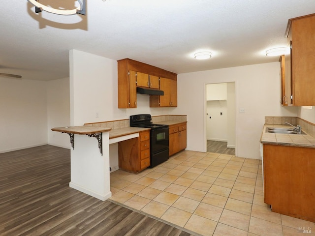 kitchen with a breakfast bar, black range with electric stovetop, sink, light wood-type flooring, and kitchen peninsula