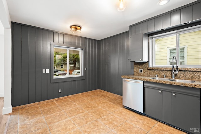 kitchen featuring decorative backsplash, stainless steel dishwasher, gray cabinetry, wooden walls, and sink