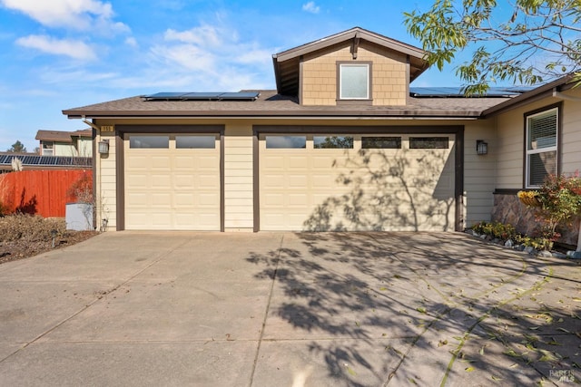 view of front of property featuring concrete driveway, fence, an attached garage, and solar panels