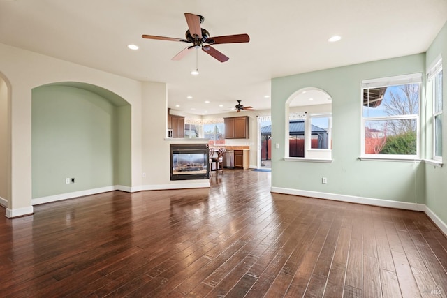 unfurnished living room with recessed lighting, baseboards, dark wood-type flooring, and a multi sided fireplace