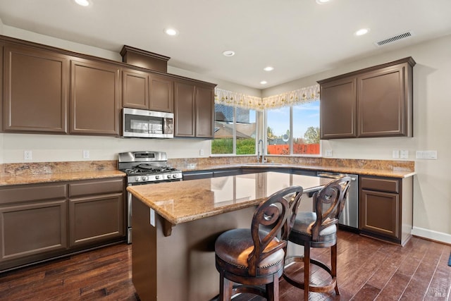 kitchen featuring stainless steel appliances, a breakfast bar, visible vents, light stone countertops, and dark wood finished floors