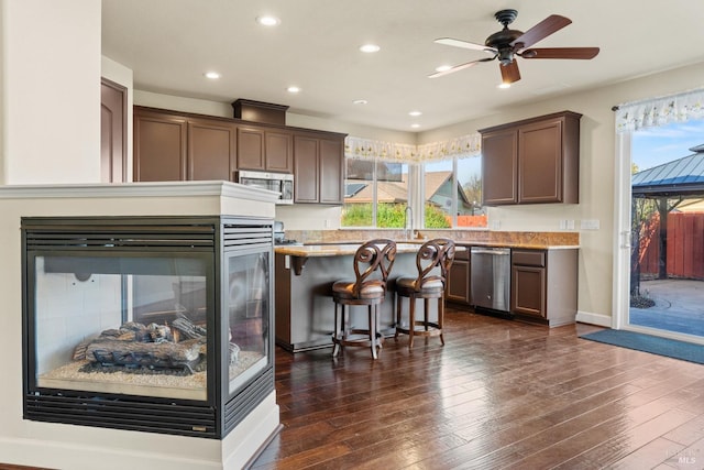 kitchen with light stone counters, a breakfast bar area, recessed lighting, appliances with stainless steel finishes, and dark wood finished floors