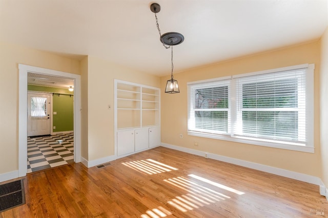 unfurnished dining area featuring built in shelves, a wealth of natural light, and wood-type flooring