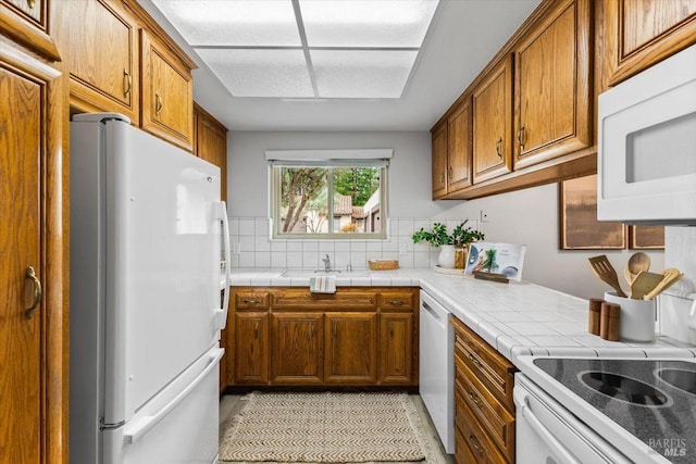 kitchen featuring tile countertops, light tile patterned flooring, white appliances, decorative backsplash, and brown cabinetry