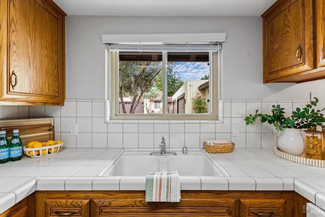 kitchen with tile counters, brown cabinets, a sink, and backsplash