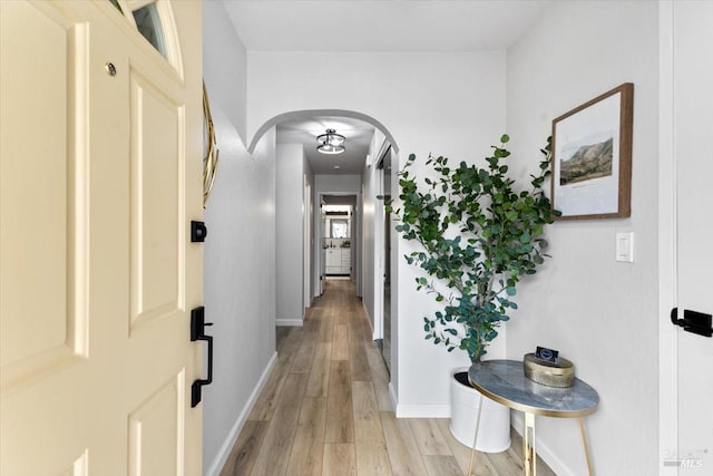 corridor with arched walkways, light wood finished floors, and baseboards