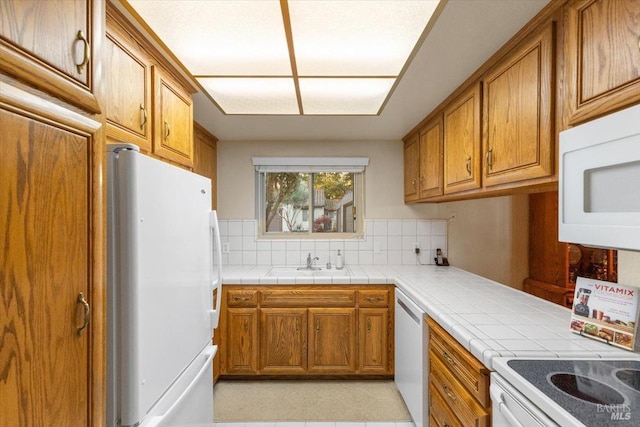 kitchen featuring backsplash, tile counters, white appliances, and sink