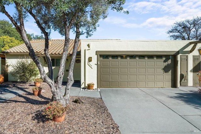 view of front facade with a garage, driveway, a tiled roof, and stucco siding