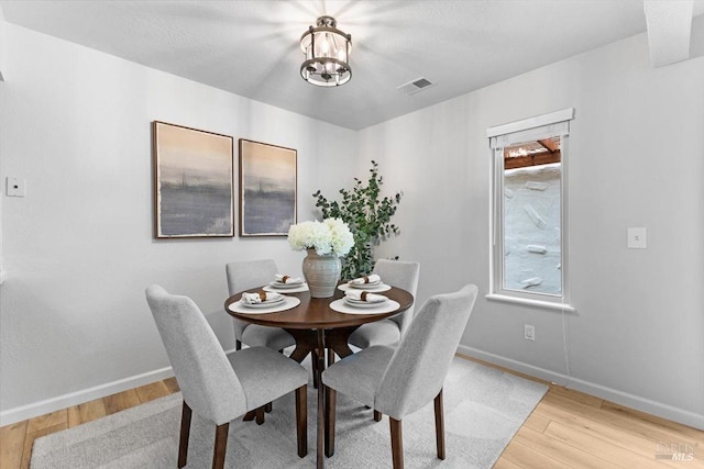 dining room featuring baseboards, visible vents, light wood finished floors, and an inviting chandelier