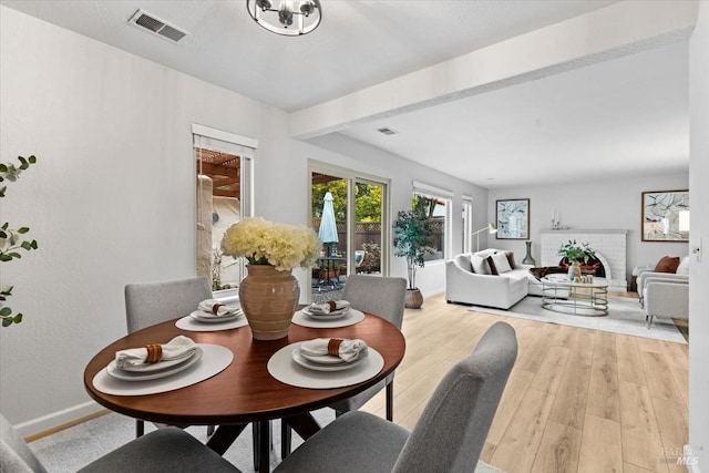 dining space with light wood-type flooring, baseboards, visible vents, and beamed ceiling