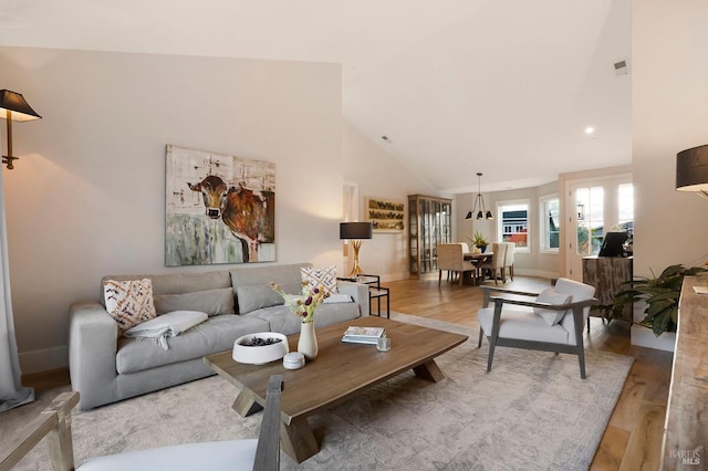 living area with high vaulted ceiling, baseboards, wood finished floors, and visible vents