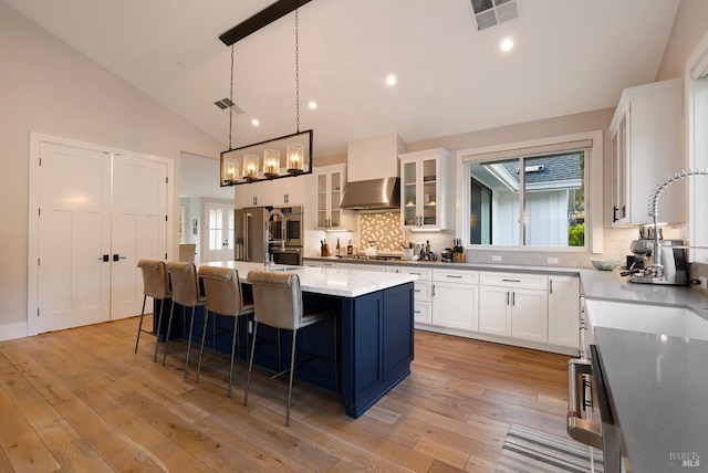 kitchen featuring wall chimney exhaust hood, visible vents, backsplash, and white cabinetry