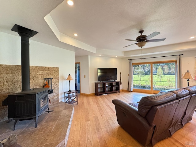 living room featuring ceiling fan, a wood stove, a textured ceiling, and light hardwood / wood-style floors