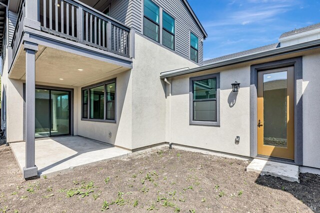 entrance to property with stucco siding, a patio area, and a balcony