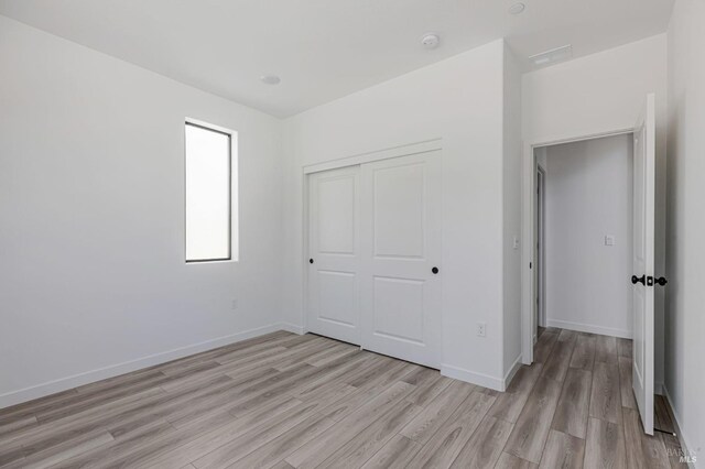 unfurnished bedroom with baseboards, a closet, light wood finished floors, and visible vents