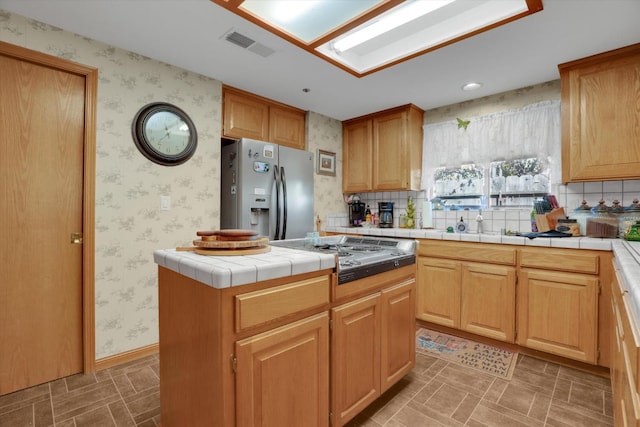 kitchen featuring tile counters, visible vents, appliances with stainless steel finishes, a kitchen island, and wallpapered walls