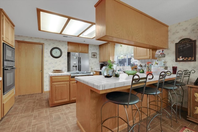 kitchen with wallpapered walls, tile countertops, a breakfast bar area, a peninsula, and black appliances