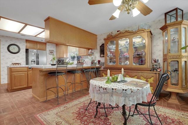 kitchen featuring a peninsula, tile counters, black appliances, a kitchen bar, and wallpapered walls